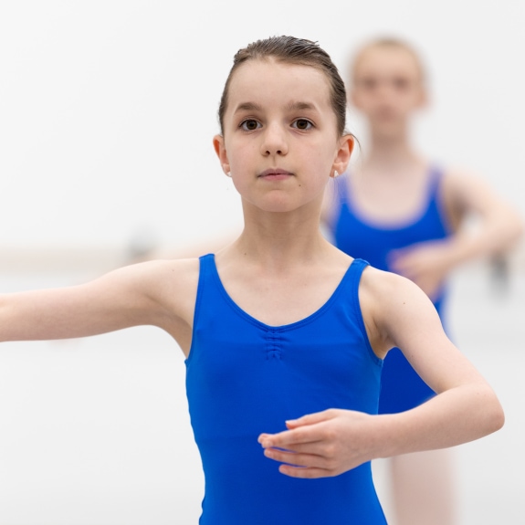a child, in a blue leotard, preparing to do a pirouette