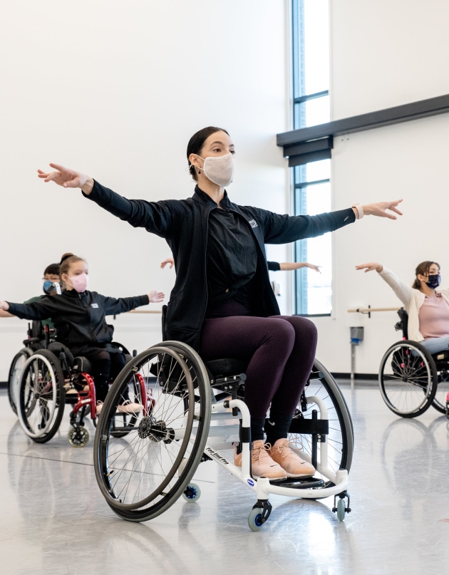 a group of people in wheelchairs with masks, dancing in the studio