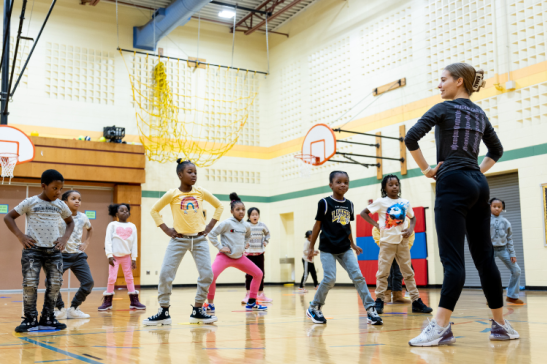 Students in a school gym imitate a dance instructor.