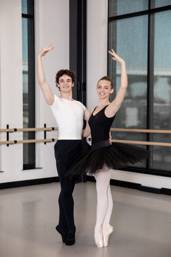 Male and female ballet dancers pose together with arms up