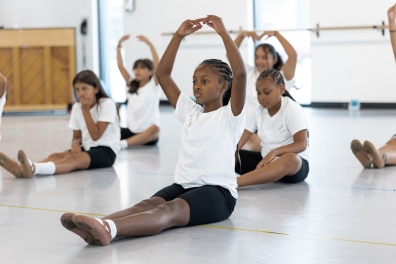 Kids sit together and practice ballet moves.
