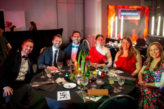 A group of six people smile at their table at the Ballet Ball.