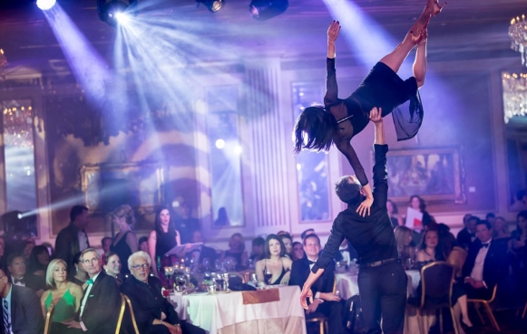 a male dancer lifting a female dancer over his head, while she holds a side plank