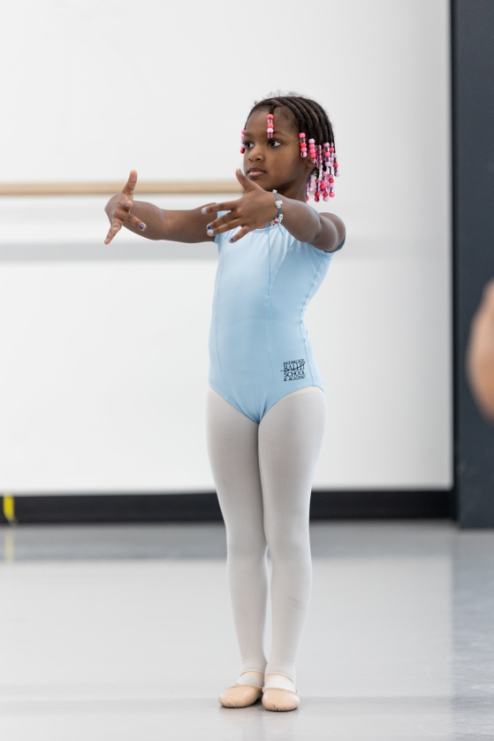 a child wearing ballet clothes and standing in first position