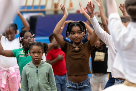 Children watch their instructor and stretch.