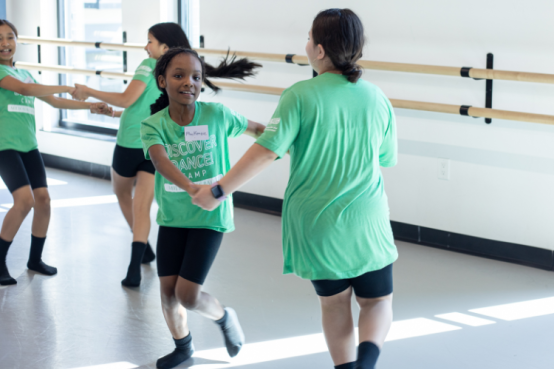 Two students dance together holding hands in the studio.