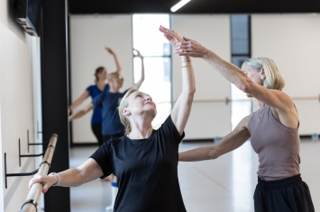 Dance instructor helps stretch a participant on barre.